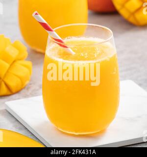 Frischer Mangosaft. Nahaufnahme des Designkonzepts eines kalten Smoothie-Getränks in einer Glasschale mit Papierstroh auf grauem Tischhintergrund. Stockfoto