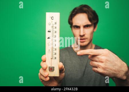 Nahaufnahme junger Mann zeigt auf Thermometer, isoliert auf grünem Hintergrund Stockfoto