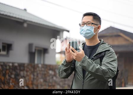 Der junge Backpacker-Mann reist allein und nutzt Smartphone, um mit Maske, Brille einen Weg zu finden. Stockfoto
