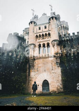 Vertikale Aufnahme der Burg Butron in Bizkaia, Spanien an einem regnerischen Tag, bei dem ein Mädchen sie ansah. Stockfoto