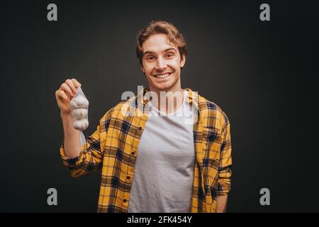 Der junge blonde Mann in gelbem Hemd hält Gurken mit einem Lächeln, isoliert auf schwarzem Hintergrund Stockfoto