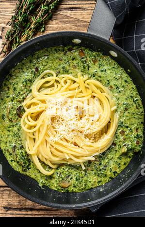 Spaghetti mit Spinat in Sahnesauce mit Parmesan in einer Pfanne. Holzhintergrund. Draufsicht Stockfoto