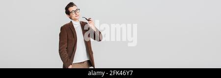 Altmodischer Mann, der die Kamera anschaut, während er mit einer rauchenden Pfeife auf einem grauen Banner posiert Stockfoto