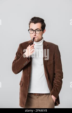 Altmodischer Mann, der Pfeife raucht, während er mit der Hand dasteht Tasche isoliert auf grau Stockfoto