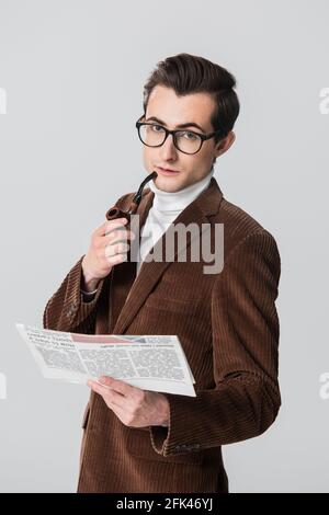 Junger Mann in Samtblazer mit Rauchpfeife und Zeitung Isoliert auf Grau Stockfoto