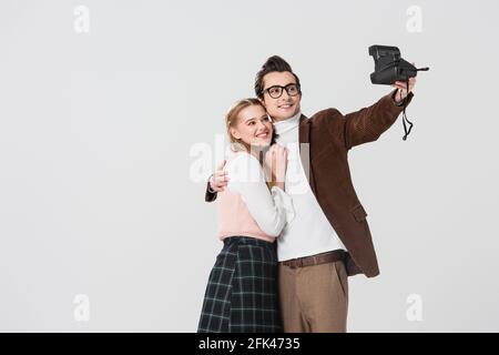 Glücklicher Mann umarmt Freundin während der Aufnahme Selfie auf Vintage-Kamera Isoliert auf Grau Stockfoto