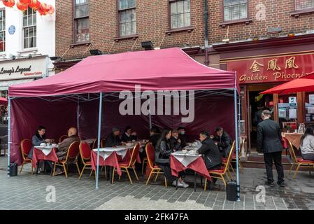 London, Großbritannien. 28. April 2021. UK Wetter: Menschen speisen außerhalb von Restaurants in Chinatown, da Einschränkungen durch Coronaviren das Essen im Inneren vorerst verhindern. Restaurantbesitzer haben Vordächer installiert, um bei schlechtem Wetter Schutz zu bieten, aber die üblichen Duschen im April waren in diesem Jahr selten. Es wird jedoch erwartet, dass in dieser Woche Regen eintreffen wird. Kredit: Stephen Chung / Alamy Live Nachrichten Stockfoto