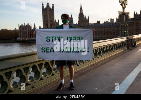 London, Großbritannien. April 2021. Greenpeace-Protestler in schützender Gesichtsmaske steht am 26. April 2021 vor Westminster, London, England mit dem Banner „Stop deep Sea Mining“. Quelle: SIPA USA/Alamy Live News Stockfoto