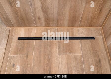 Moderner schwarzer linearer Abfluss in einem Badezimmer mit Keramikfliesen, die Holz imitieren. Stockfoto