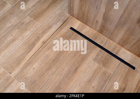 Moderner schwarzer linearer Abfluss in einem Badezimmer mit Keramikfliesen, die Holz imitieren. Stockfoto