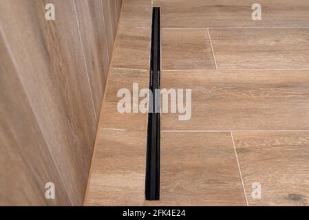Moderner schwarzer linearer Abfluss in einem Badezimmer mit Keramikfliesen, die Holz imitieren. Stockfoto