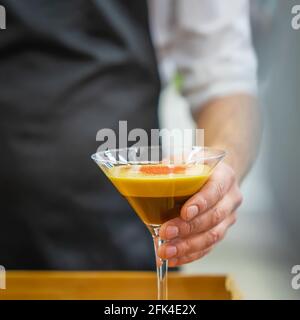 Hand des Barista hält ein Glas Espresso-Kaffee-Cocktail aus der Nähe. Alkoholische und alkoholfreie Erfrischungsgetränke Stockfoto