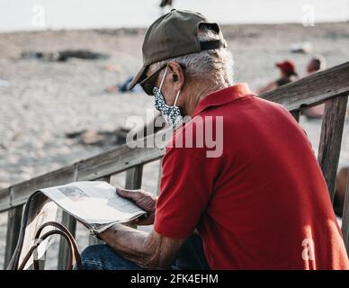 Shallow-Focus-Aufnahme eines alten Mannes beim Lesen der Zeitung Draußen am Strand Stockfoto