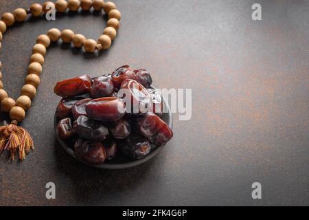 Ramadan. Hölzerne Gebetskugeln und Datteln in Schale auf braun. Blick von oben. Eid Mubarak. Religiöse Tradition. Stockfoto