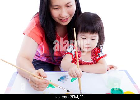 Porträt einer Frau und eines kleinen asiatischen (thailändischen) Mädchens, das zeichnet und malt, Mutter lehrt ihre Tochter, mit einem Pinsel zu zeichnen, isoliert auf weißem Hintergrund. Stockfoto