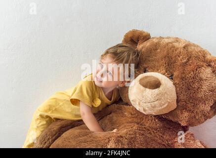 Süßer, fröhlicher Junge, der mit seinem riesigen Teddybären spielt, drinnen zu Hause Stockfoto