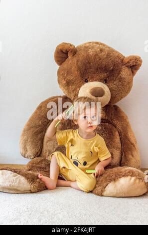 Süßer, fröhlicher Junge, der mit seinem riesigen Teddybären spielt, drinnen zu Hause Stockfoto