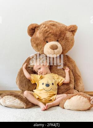 Süßer, fröhlicher Junge, der mit seinem riesigen Teddybären spielt, drinnen zu Hause Stockfoto