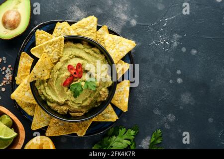 Guacamole. Traditionelle lateinamerikanische mexikanische Dip-Sauce in einer schwarzen Schüssel mit Avocado und Zutaten und Maisnachos. Avocadoverbreitung. Draufsicht. Copyspa Stockfoto