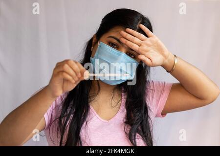 Selektiver Fokus auf eine mittelErwachsene indische Frau, die eine chirurgische Nasenmaske und ein analoges Thermometer in der Hand trägt, Gesundheitskonzept Stockfoto