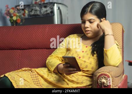 Eine indische asiatische hübsche Frau mit Smartphone sitzend auf Sofa Stockfoto