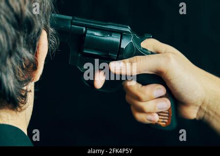 Die Waffe wird an den Kopf des Menschen gehalten. Mord an einer Person, indem sie ihn mit einer Schusswaffe im Kopf erschießt hat. Männlich will mit Pistole schießen. Stockfoto