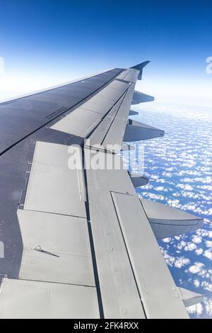 Der Blick aus dem Fenster eines Düsenflugzeugsflügels Blick hinunter auf einen blauen Himmel mit flauschigen weißen Wolken Stockfoto