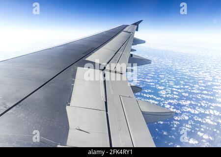 Der Blick aus dem Fenster eines Düsenflugzeugsflügels Blick hinunter auf einen blauen Himmel mit flauschigen weißen Wolken Stockfoto