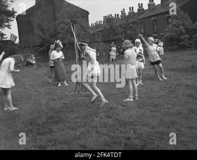 Die 50er Jahre, historisch, auf einem Stück Land am Ende der Terrasse viktorianischer Hütten, eine Gruppe von lokalen Männern - "The Heavy Gang" in Frauen gekleidet tanzen um eine Maypole, England, Großbritannien. Der Maifeiertag war eine uralte Tradition, die die Ankunft von Frühling und Sommer feierte, und Darsteller reenact alte Folklore und Musik, mit dem Springen um einen hohen hölzernen Pol, ein Maibaum, eine der populären Feier Aktivitäten. Stockfoto