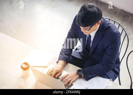 Draufsicht auf den Mann, der mit dem Unternehmen am Laptop tippt Dokumente auf dem Bürotisch Stockfoto