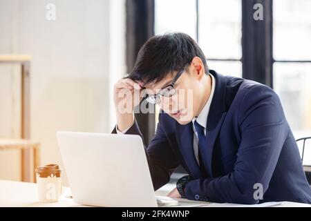 Besorgt und enttäuscht Remote online arbeitenden Mann in lässigem Outfit Mit Laptop sitzt in einem Coworking / Home Office bei Ein Schreibtisch Stockfoto