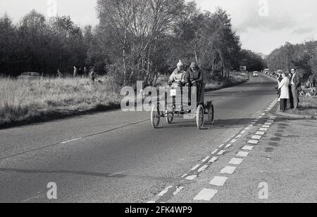 In den 1980er Jahren, auf einer Straße mit zwei Wagen, fahren zwei Männer in einem alteingesessenen Auto, das an der historischen jährlichen Autofahrt, dem Veteran Car Run von London nach Brighton, teilnimmt, der vom RAC organisiert wird. Die längste Motorveranstaltung der Welt steht nur Automobilen offen, die vor 1905 gebaut wurden. Der erste Automobilclub im Vereinigten Königreich wurde 1896 gegründet, der die Light Locomotives on the Highway Act feierte, der die Geschwindigkeitsbegrenzung auf 14 km/h erhöhte und die Notwendigkeit für Autos abschaffte, denen ein Mann zu Fuß mit einer roten Flagge vorausging. Stockfoto