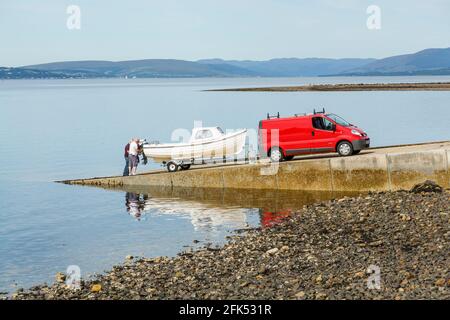 Zwei Männer auf einem Slipway, die sich darauf vorbereiten, in einem kleinen Boot zu segeln, Schottland, Großbritannien Stockfoto