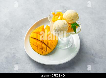 Mango-Eiskugeln und frische Mango auf einem weißen Teller auf grauem Hintergrund. Stockfoto