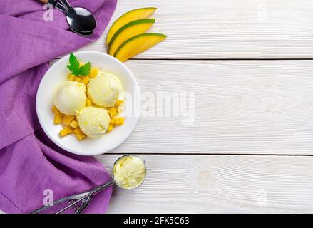 Drei Kugeln aus Mango-Eis frische Mangoscheiben auf weißem Hintergrund mit einer violetten Serviette. Stockfoto