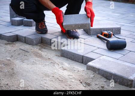 Der Meister in gelben Handschuhen legt Pflastersteine Stockfoto