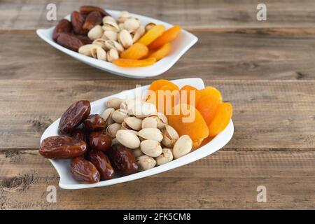 Trockenobstschale mit Datteln, Pistazien und getrockneten Aprikosen auf Holzsockel. Speicherplatz kopieren. Stockfoto