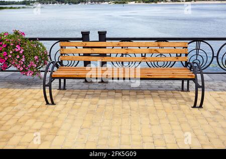 Böschung mit Bank mit Blick auf das Meer. Parken Sie die Holzbank auf dem gepflasterten Bürgersteig Stockfoto