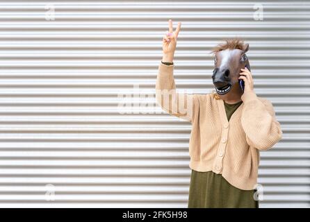 Weibliche Porträt trägt Pferdekopfmaske im Gespräch am Telefon mit Zwei Finger nach oben, Sieg sign.woman Erfolg, Feier Konzept, Werbung Lifestyle w Stockfoto