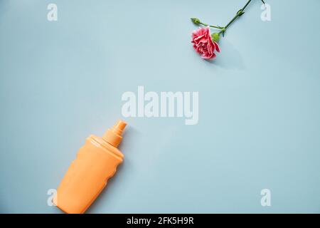 Kosmetische Flasche Nachbildung und rosa zarte Blume auf blauem Hintergrund. Eine moderne konzeptuelle weibliche Handlung. Speicherplatz kopieren. Stockfoto