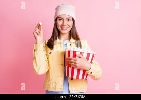 Portrait of adorable lustige Person halten Popcorn genießen Moment tragen Kappe isoliert auf rosa Hintergrund Stockfoto