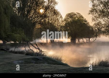 Kraft der natürlichen Welt mit aufgehender Sonne, die durch den Nebel über einem kleinen Teich brennt. Wenn ich auf öffentlichem oder privatem Grundstück bin, bin ich bereit, t Stockfoto