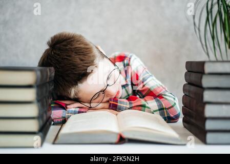 Lustiger Junge mit Brille, schlief auf einem Buch in der Bibliothek ein. Schul- und Bildungskonzept Stockfoto