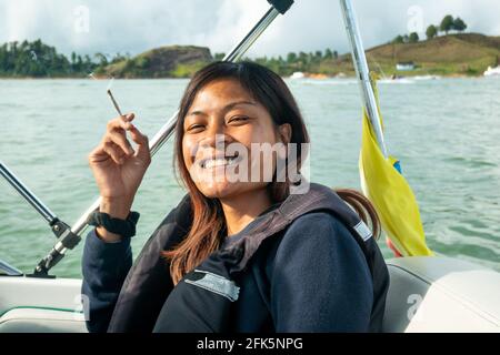 Guatapé, Antioquia, Kolumbien - April 3 2021: Asiatische Brünette raucht auf einem Boot am Staudamm eine Zigarette Stockfoto