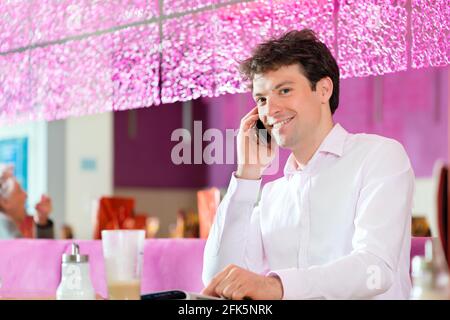 Junger Mann in einem Café oder Eis-Salon mit seinem Telefon, vielleicht ist er single oder jemand wartet Stockfoto