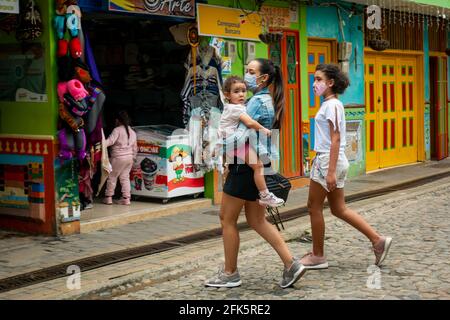 Guatapé, Antioquia, Kolumbien - April 4 2021: Latina verschiedener Altersgruppen, die Masken tragen, überqueren die Straße mit einem kleinen Mädchen in den Armen Stockfoto