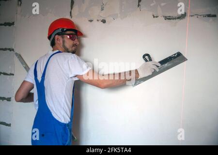 Arbeiten Sie an der Fertigstellung der Wände mit Mischungen aus Gips und Kitt beim Bau eines Hauses. bauarbeiter Verputzen Fassade des Hochhauses mit Kitt Messer. Nivellierung Steinwände Stockfoto