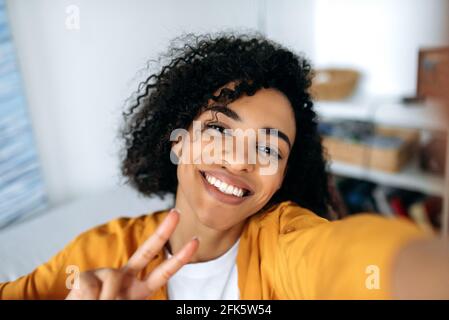 Nettes schönes, fröhliches, rothaariges afroamerikanisches Mädchen, Teenager, posiert für Selfie auf dem Smartphone, täuscht sich herum, hat Spaß, schaut auf die Telefonkamera, lächelt glücklich Stockfoto