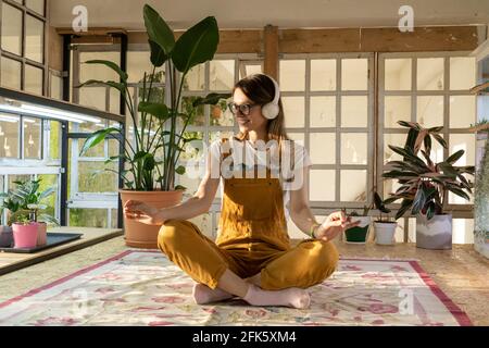 Junge Gärtnerin meditiert. Schöne Hündin im Jumpsuit und Kopfhörer entspannen vom Studium oder der Arbeit Stockfoto