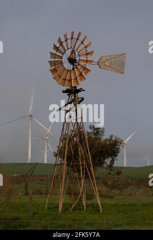 Eine legendäre, traditionelle Windmühle steht vor einer Reihe von Hightech-Windmaschinen, die auf privaten Weiden im kalifornischen Solano County aufgestellt sind. Stockfoto